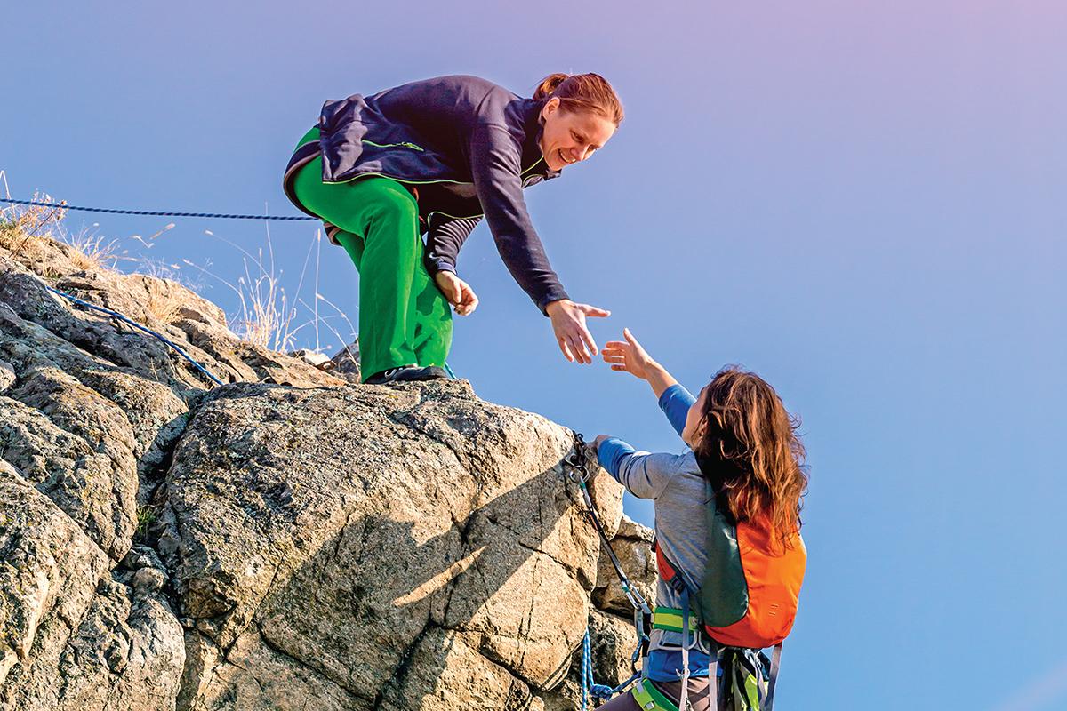 Man assisting a woman climbing over a rock face